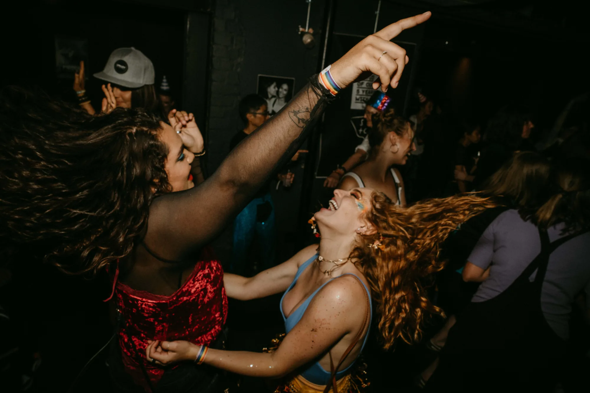 Two women with long hair dancing and laughing at a lively club event.