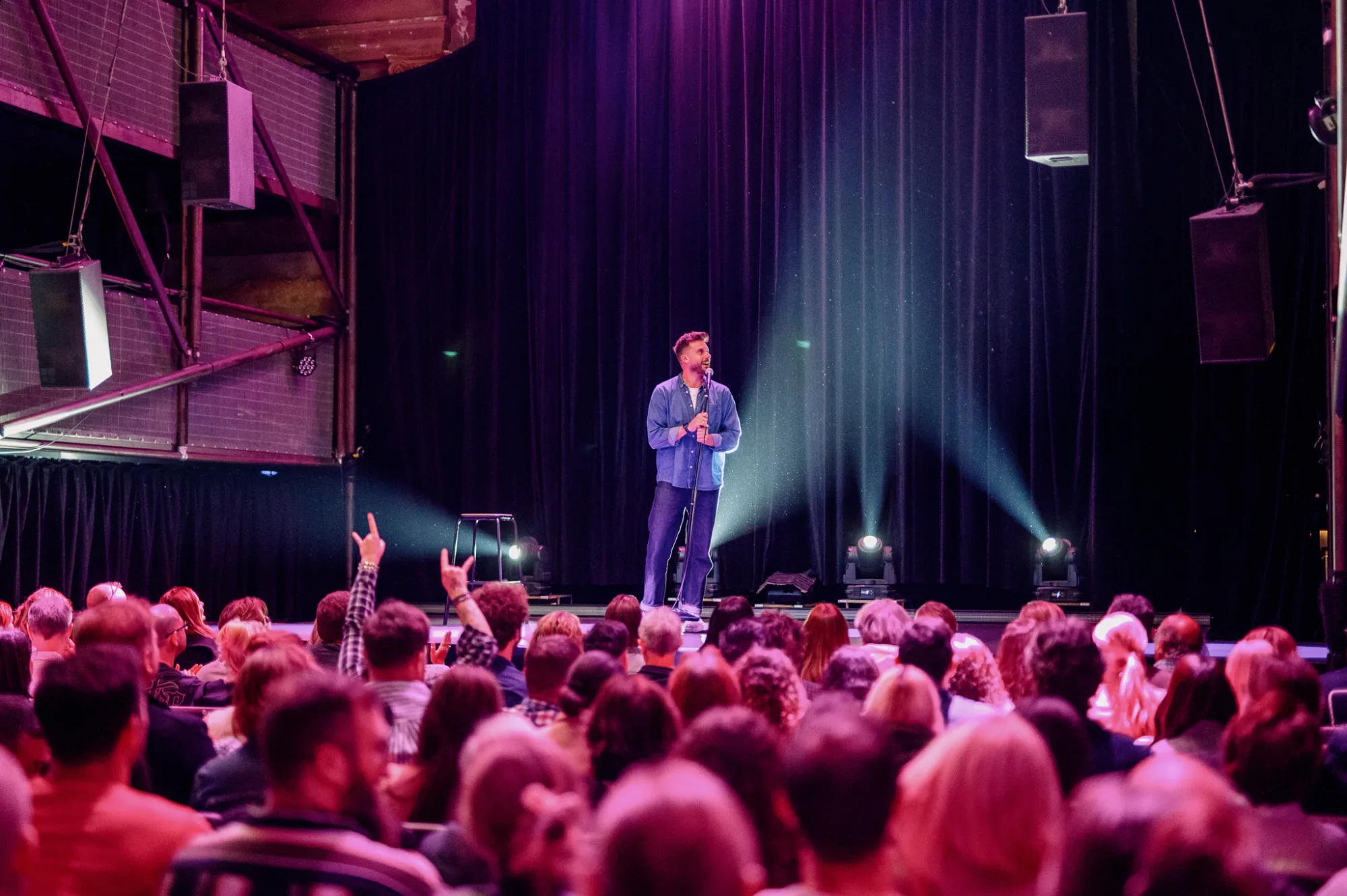 A man stands on a stage with a microphone, facing a seated audience.